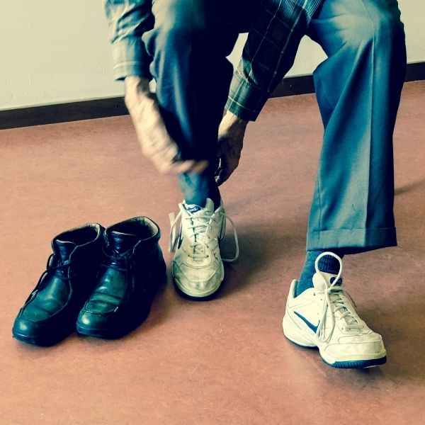 man putting on sneakers with dress shoes beside him man putting on sneakers with dress shoes beside him